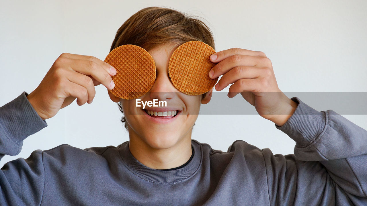 Teenage caucasian guy holding traditional dutch waffles covering his eyes having fun