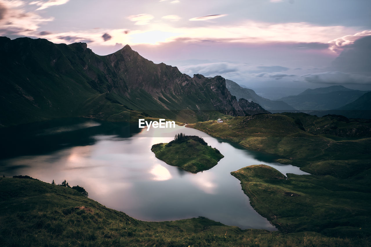 Scenic view of lake and mountains against cloudy sky during sunset