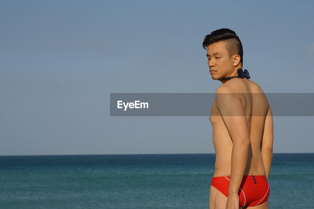 Shirtless man standing at beach against sky