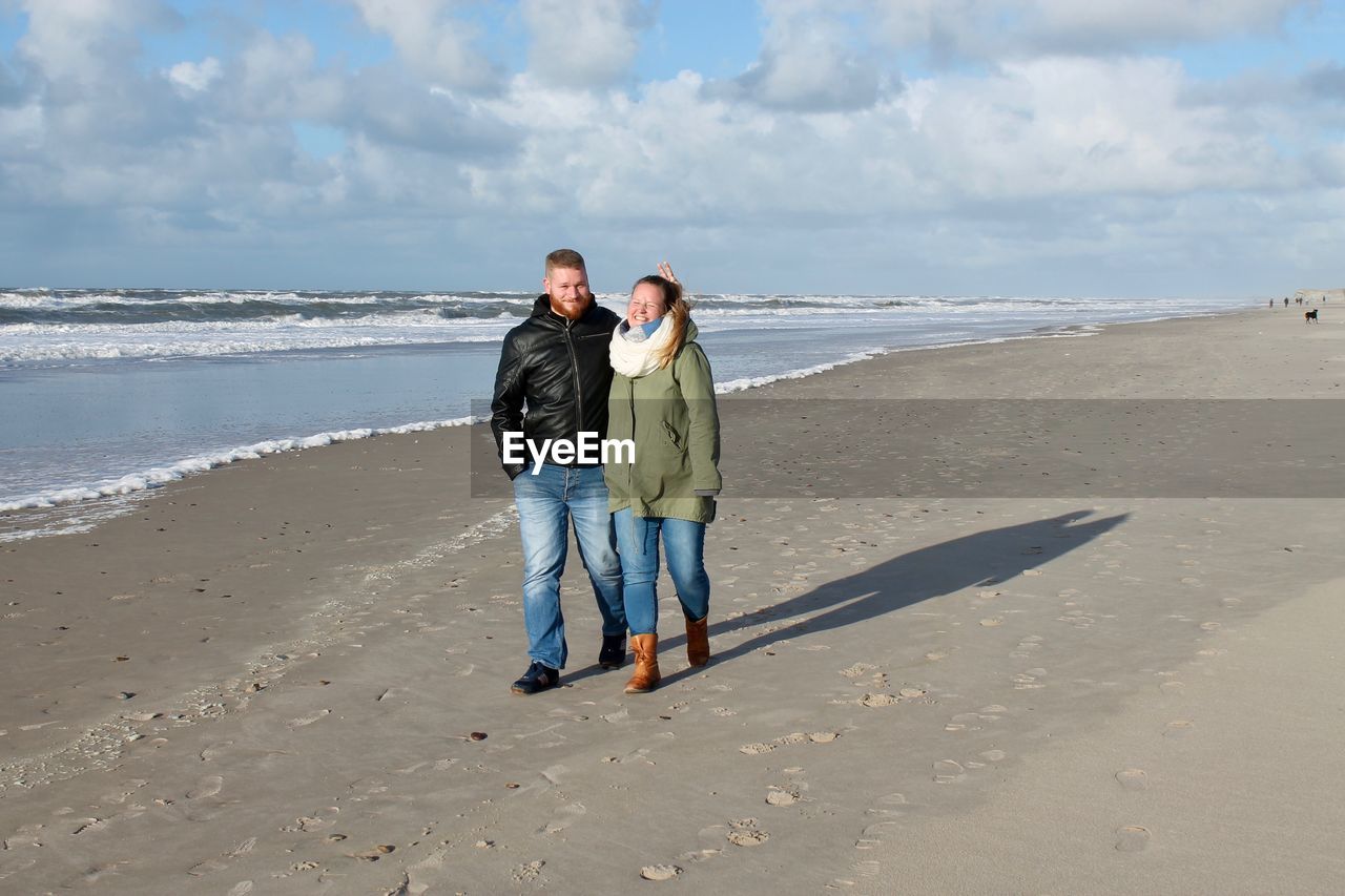 FULL LENGTH PORTRAIT OF FRIENDS STANDING ON BEACH