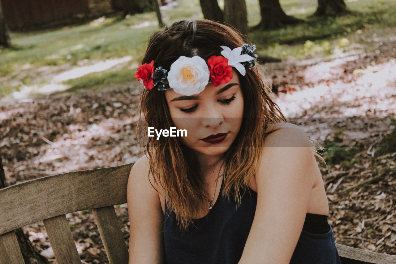 Close-up of young woman wearing flowers while sitting on bench at park