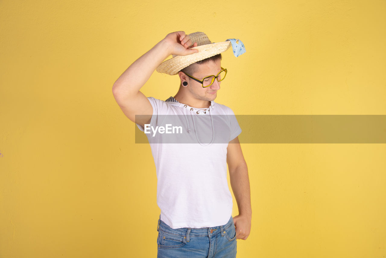 Smiling young man wearing hat standing against yellow background