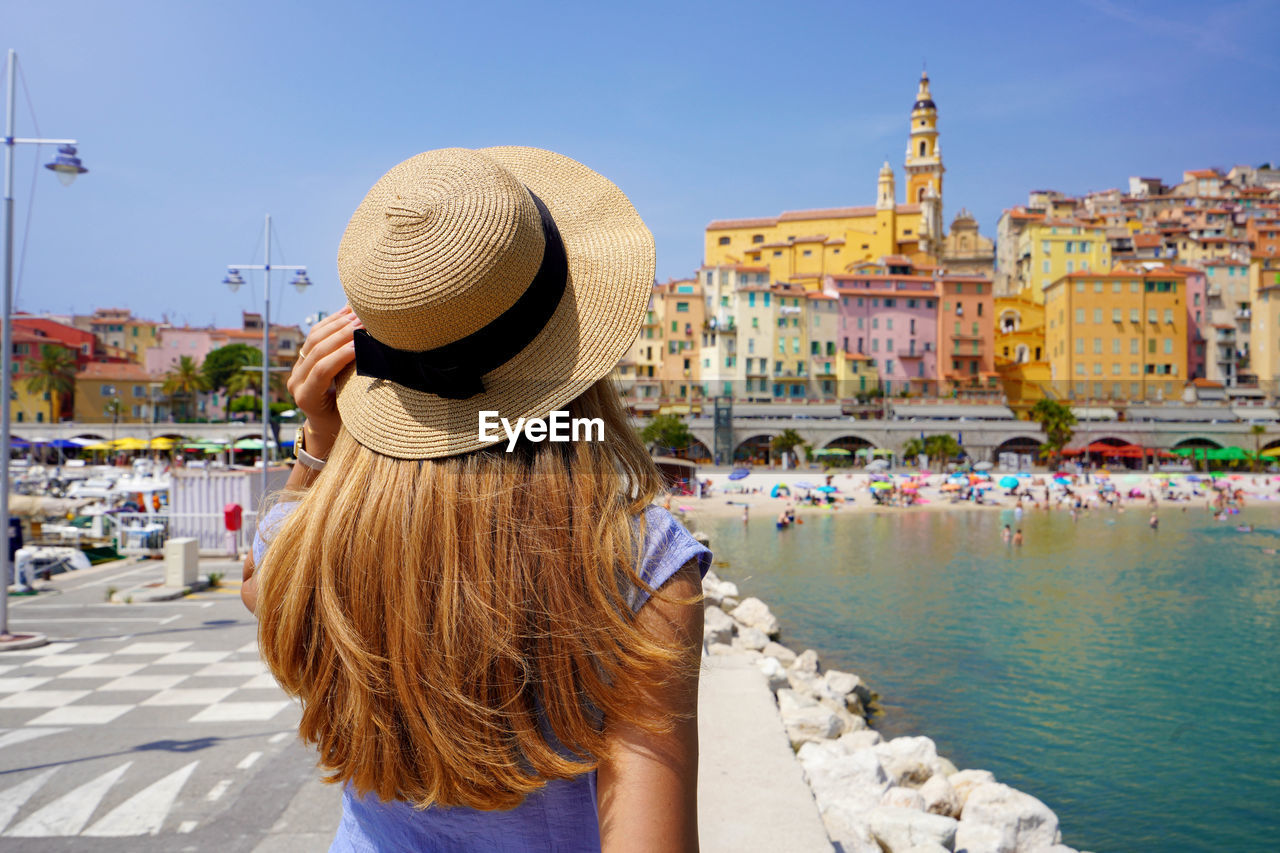 Summer holiday in france. back view of young woman with long hair and hat in menton, french riviera.