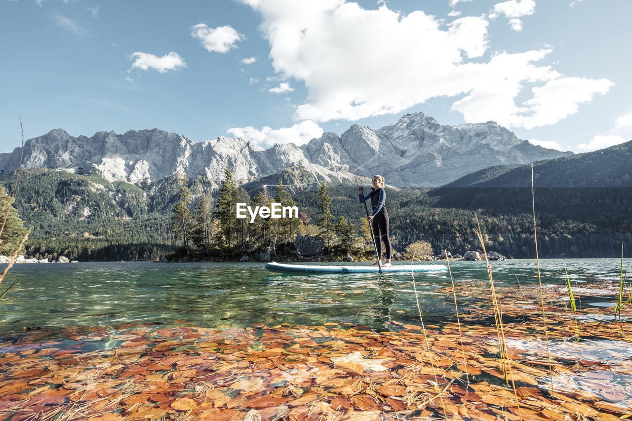 Germany, bavaria, garmisch partenkirchen, young woman stand up paddling on lake eibsee