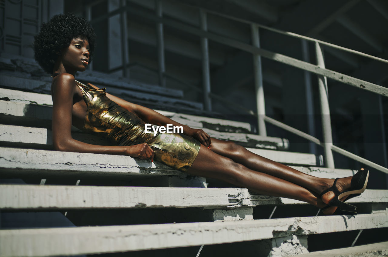 Low angle view of woman in dress looking away while sitting on steps