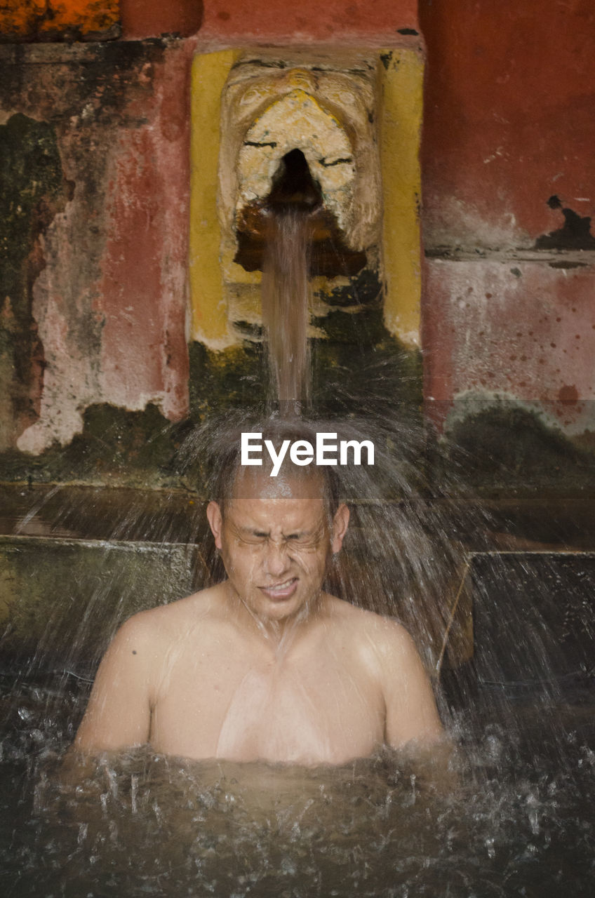 Shirtless monk taking bath in hot spring at temple