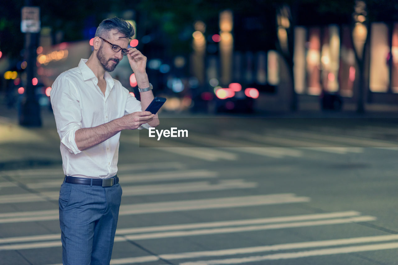 Businessman using phone while standing on street at night