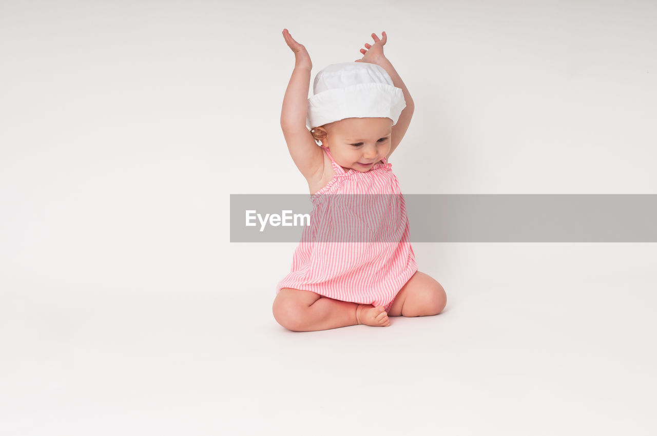 Happy baby sitting with arms up against white background