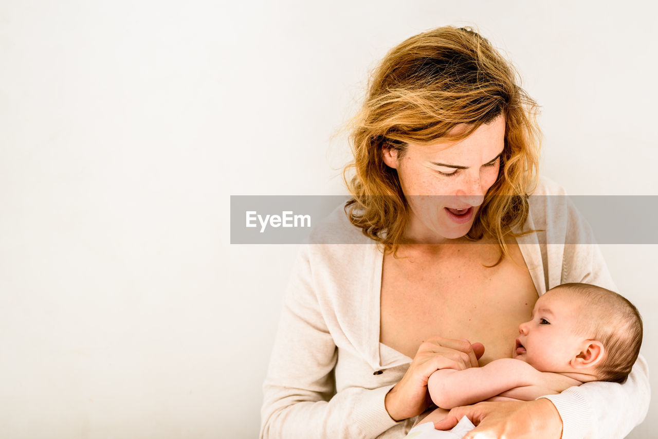 Mother breastfeeding baby against white background