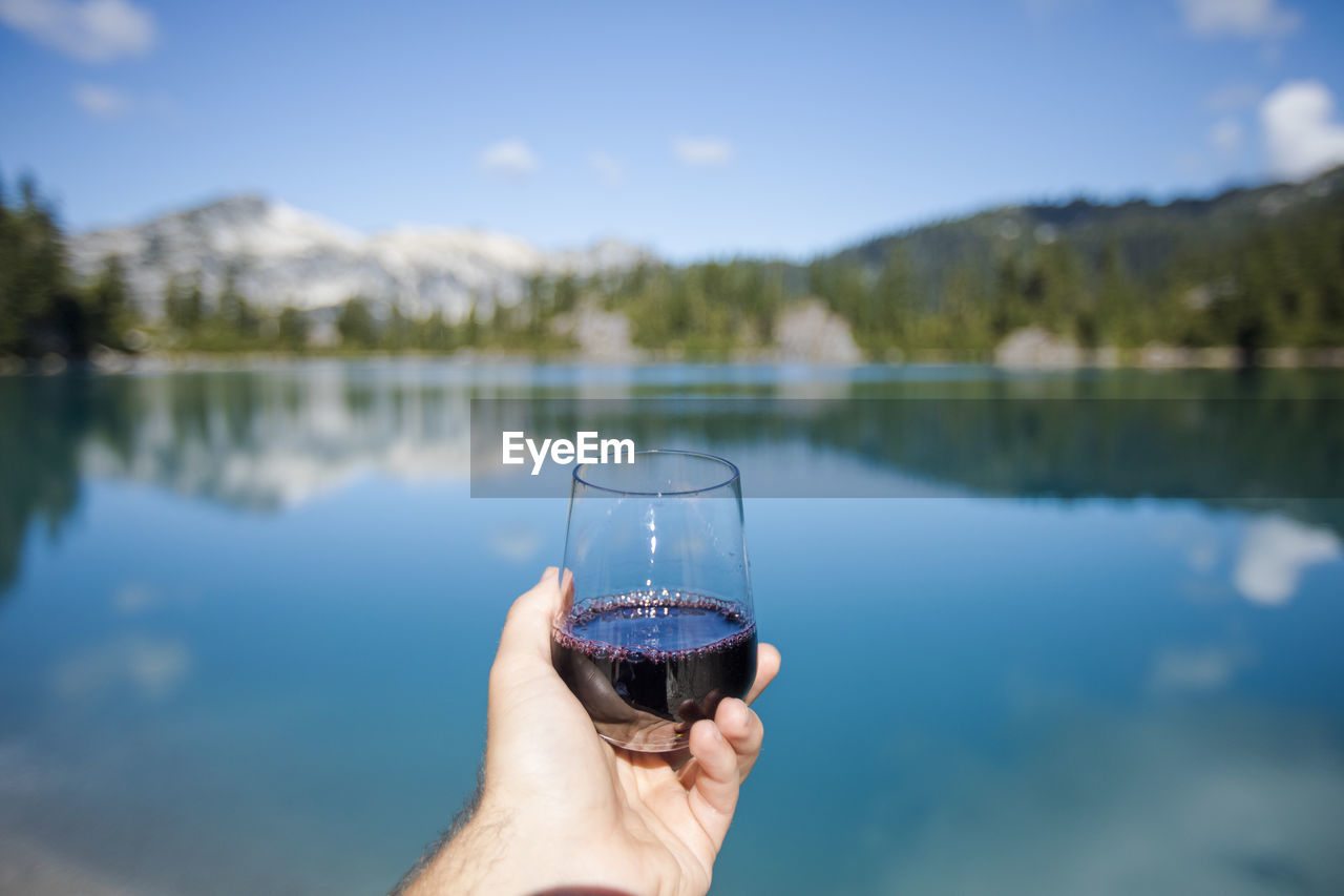 Man holds glass or red wine at the lake.