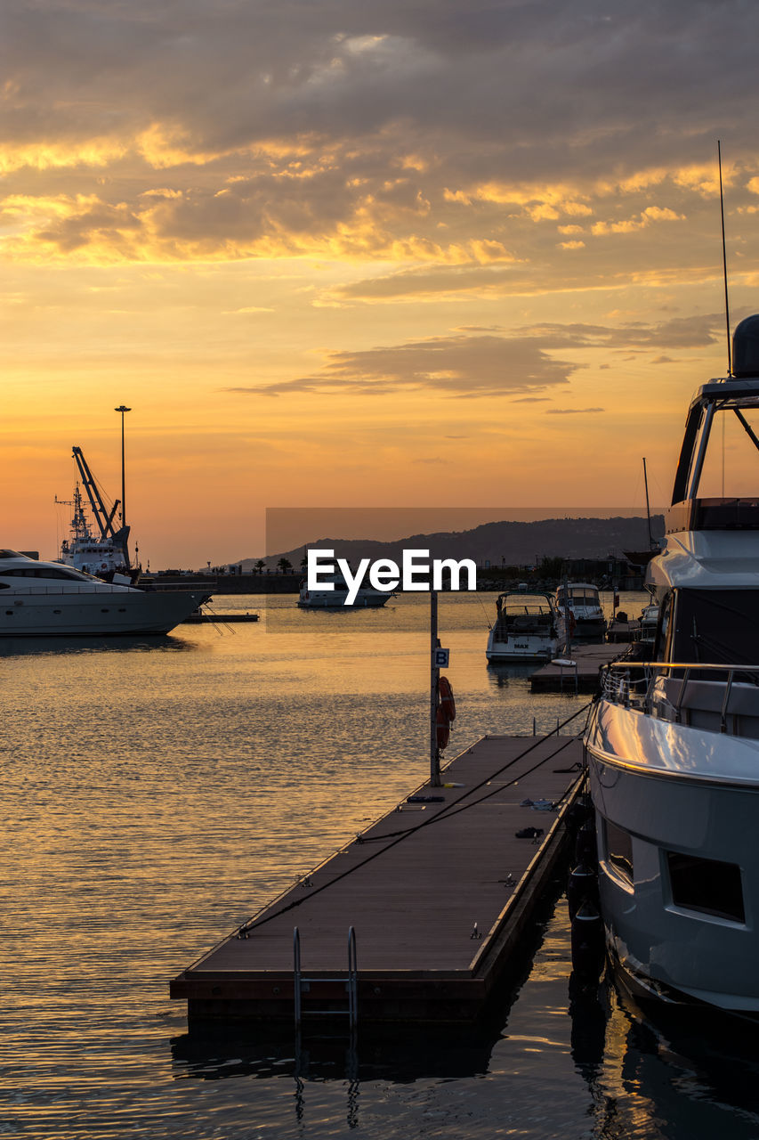 Boats moored at harbor against sky during sunset