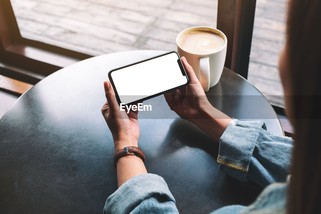 Midsection of woman using phone by coffee on table