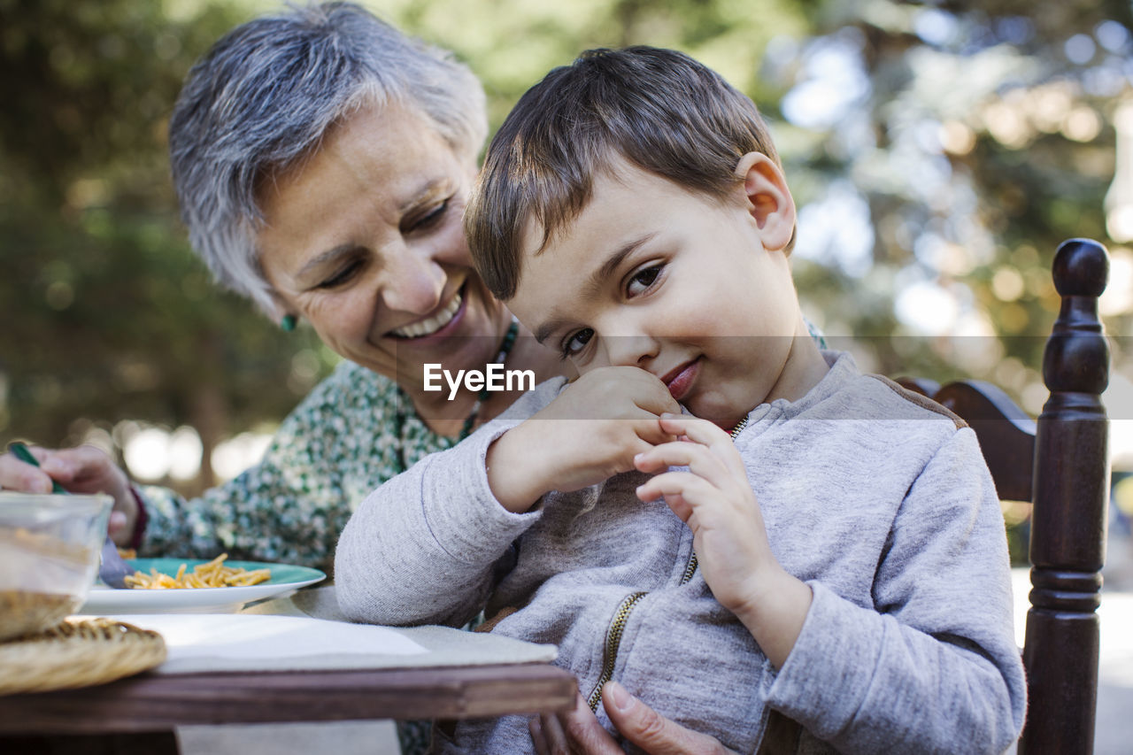 Portrait of cute boy sitting with grandmother at outdoor table