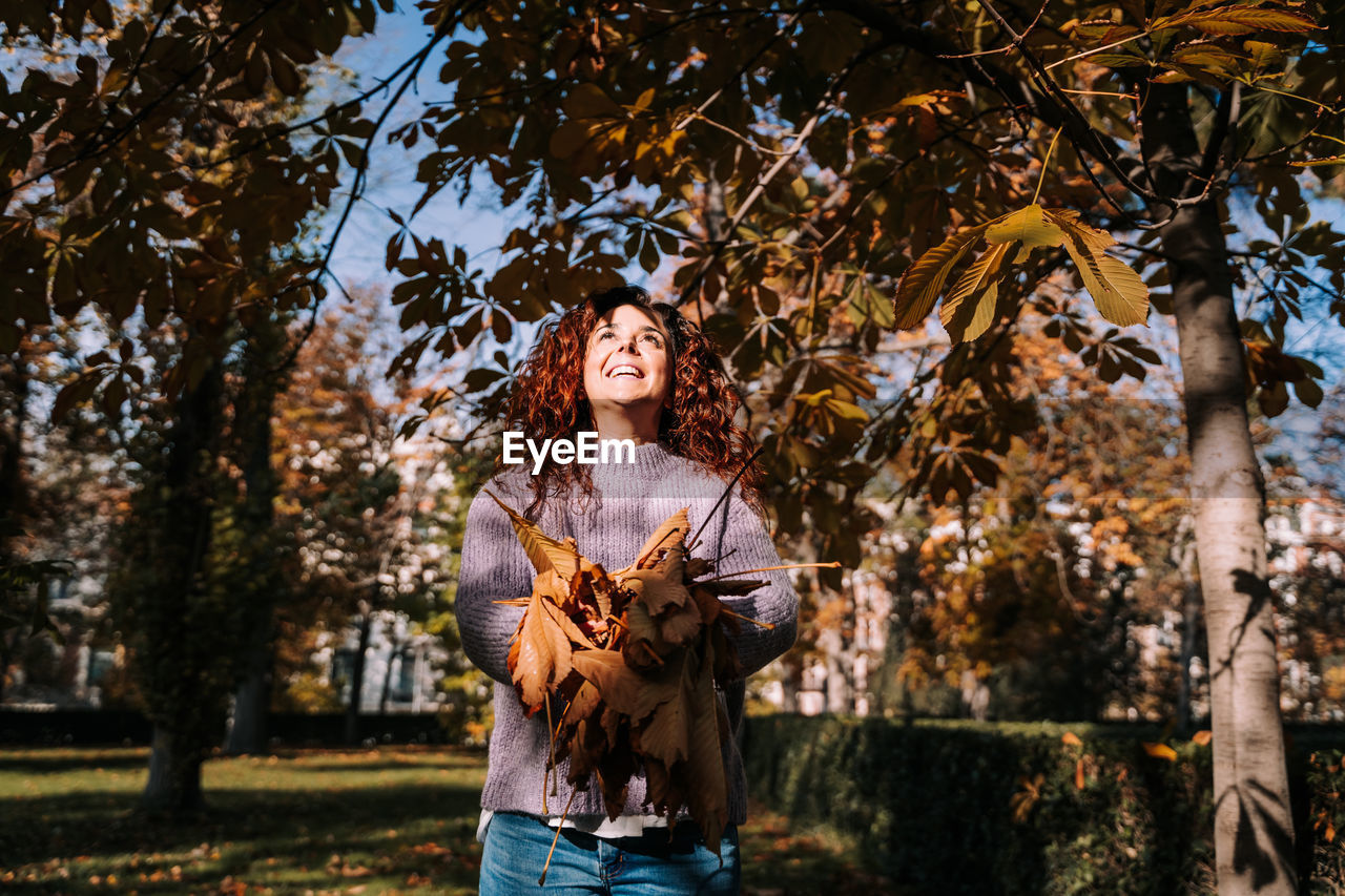 Smiling woman holding autumn leaf standing at park