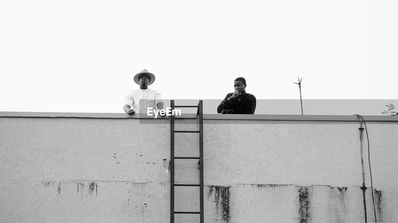 LOW ANGLE VIEW OF PEOPLE SITTING AGAINST WALL