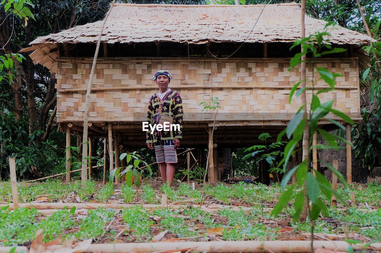 MAN STANDING BY HOUSE AGAINST PLANTS