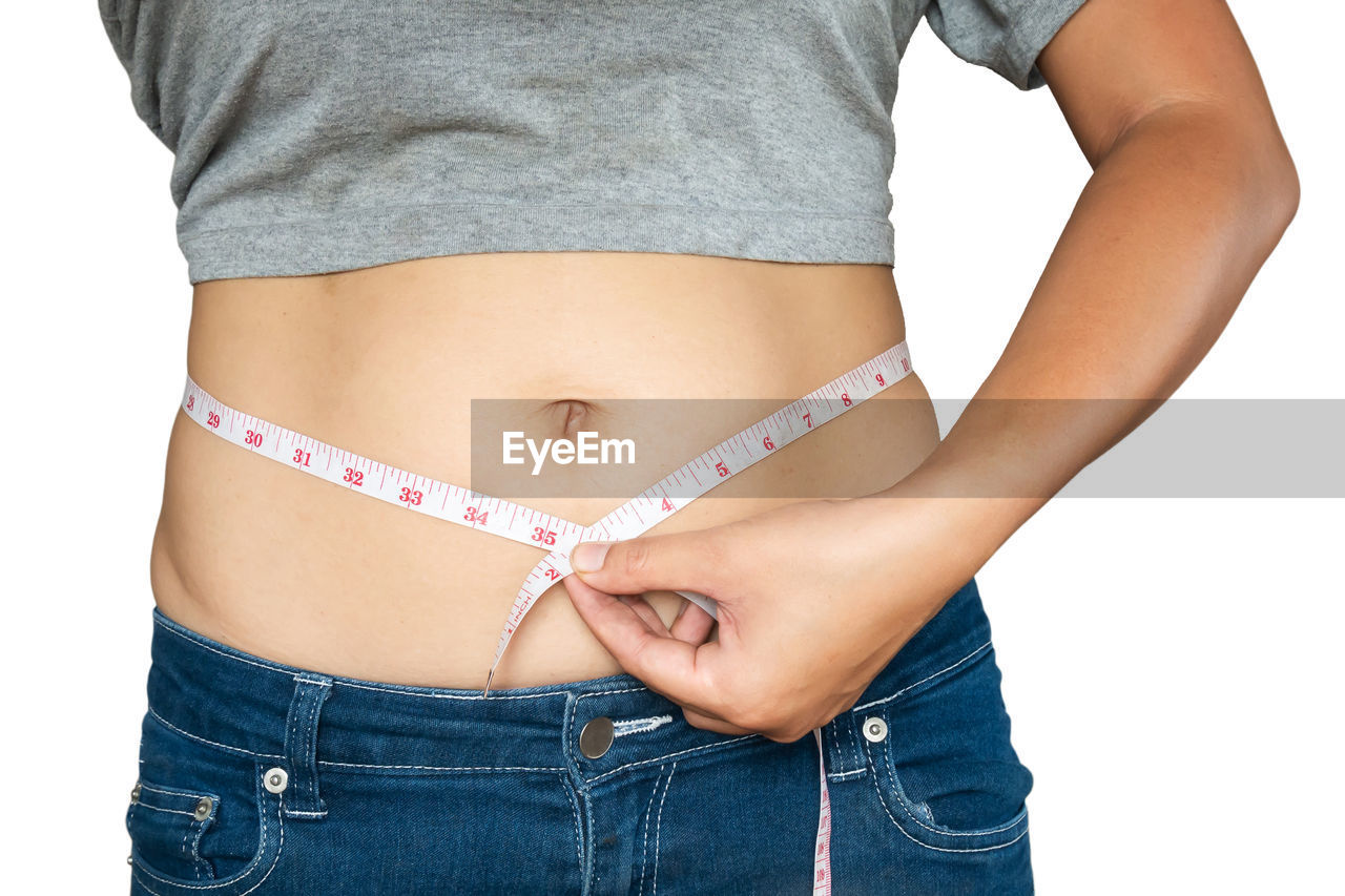 Midsection of woman measuring waist against white background