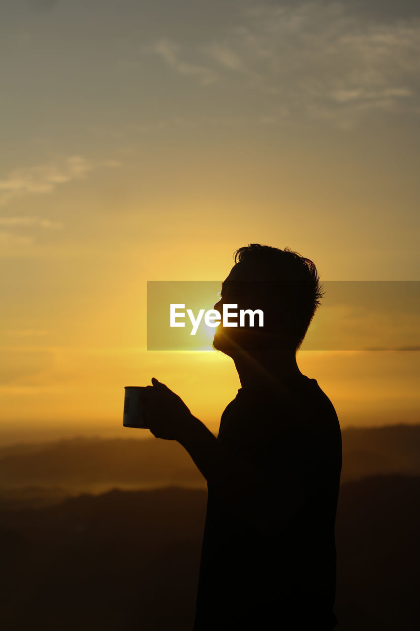 SILHOUETTE MAN STANDING AGAINST ORANGE SUNSET SKY