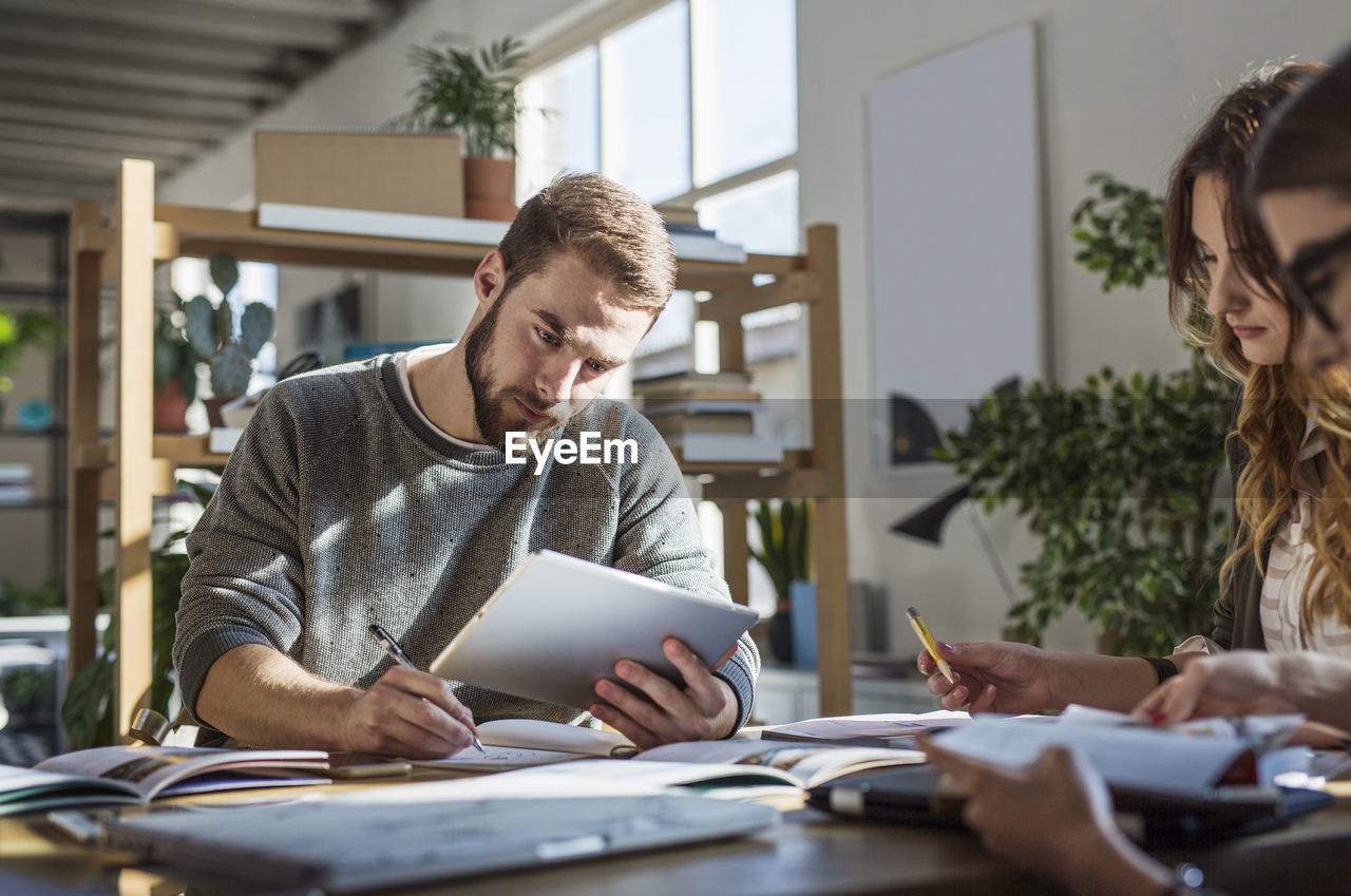 Man using tablet computer while studying with friends at table in classroom