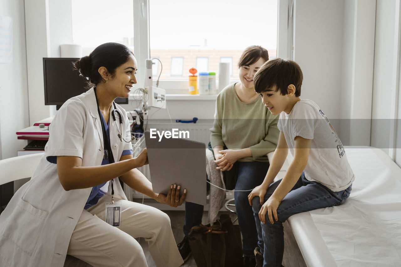 Female pediatrician showing tablet pc to mother and son sitting in examination room at clinic