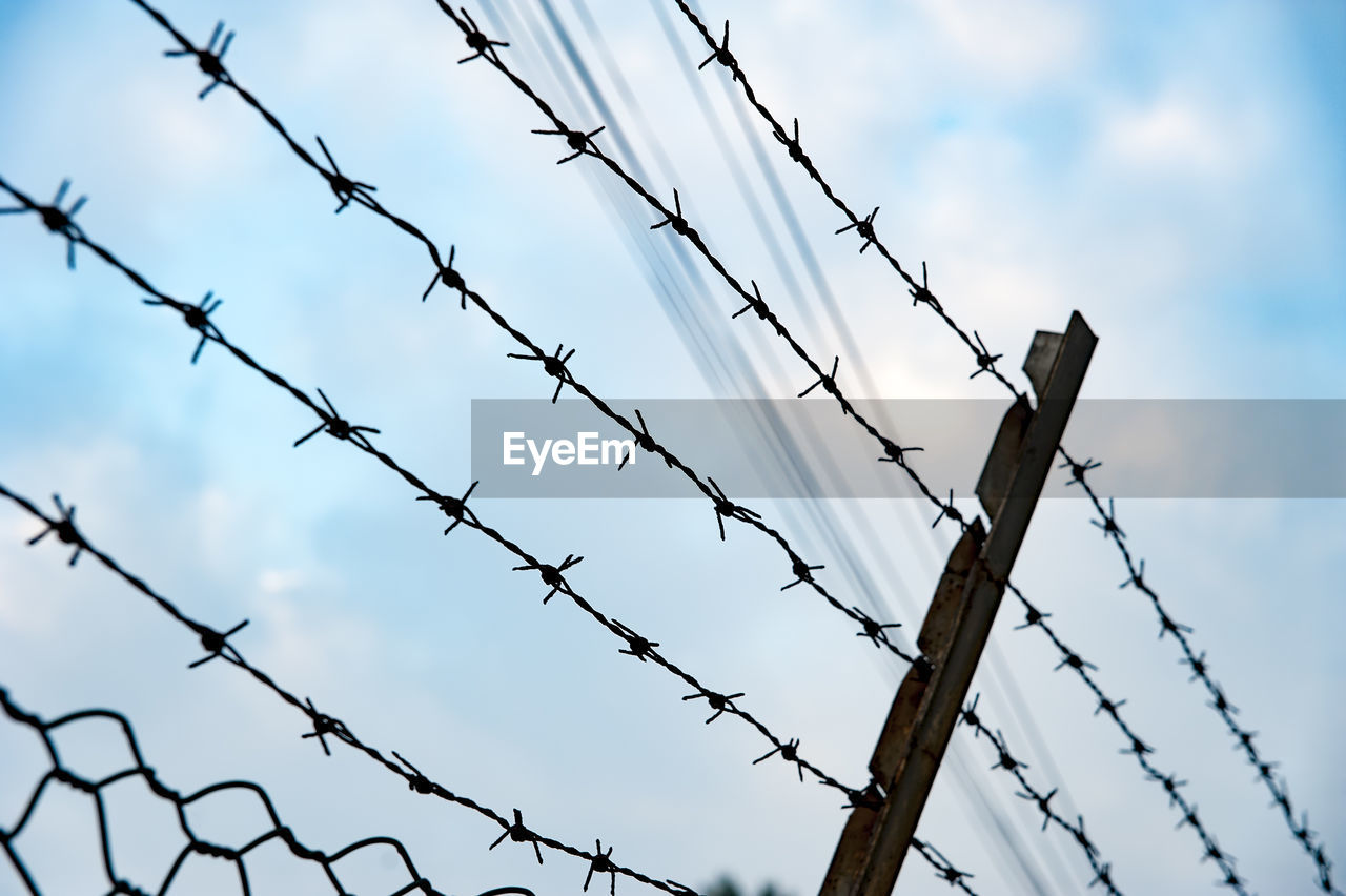 LOW ANGLE VIEW OF BARBED WIRE AGAINST FENCE