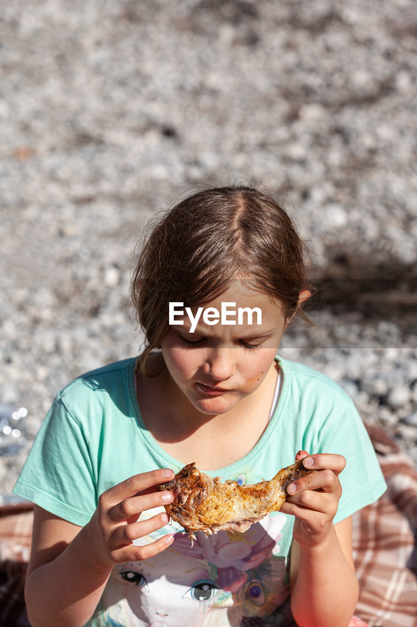 Young girl with a chicken leg in her hand at a picnic .