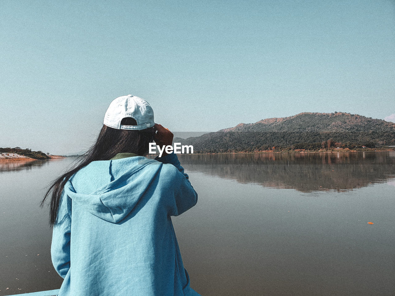 Rear view of woman looking at lake against clear sky