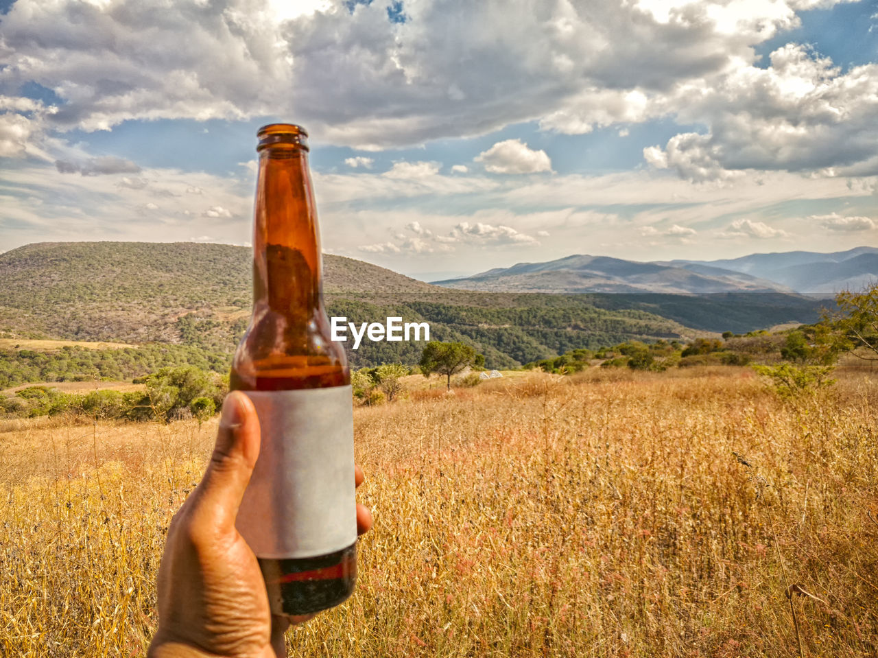 A hand is holding a beer bottle with blank label on the mountainside. travel in guerrero, mexico.