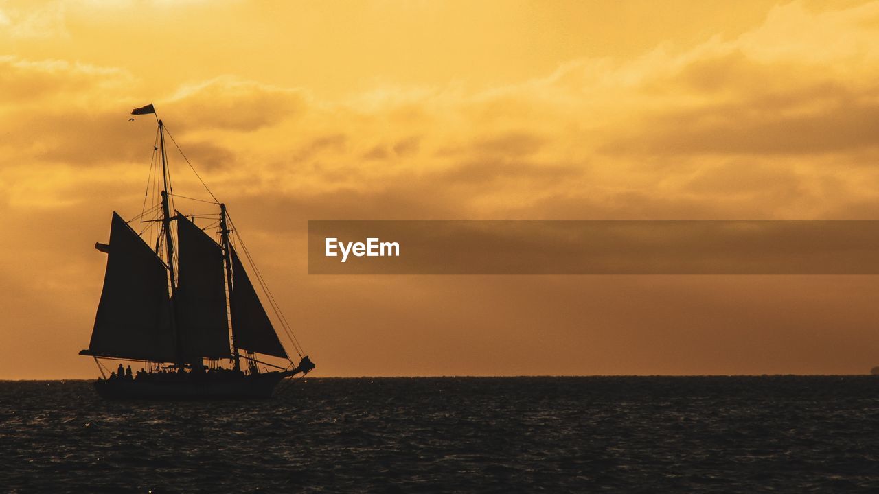 SAILBOAT SAILING IN SEA AGAINST SKY AT SUNSET