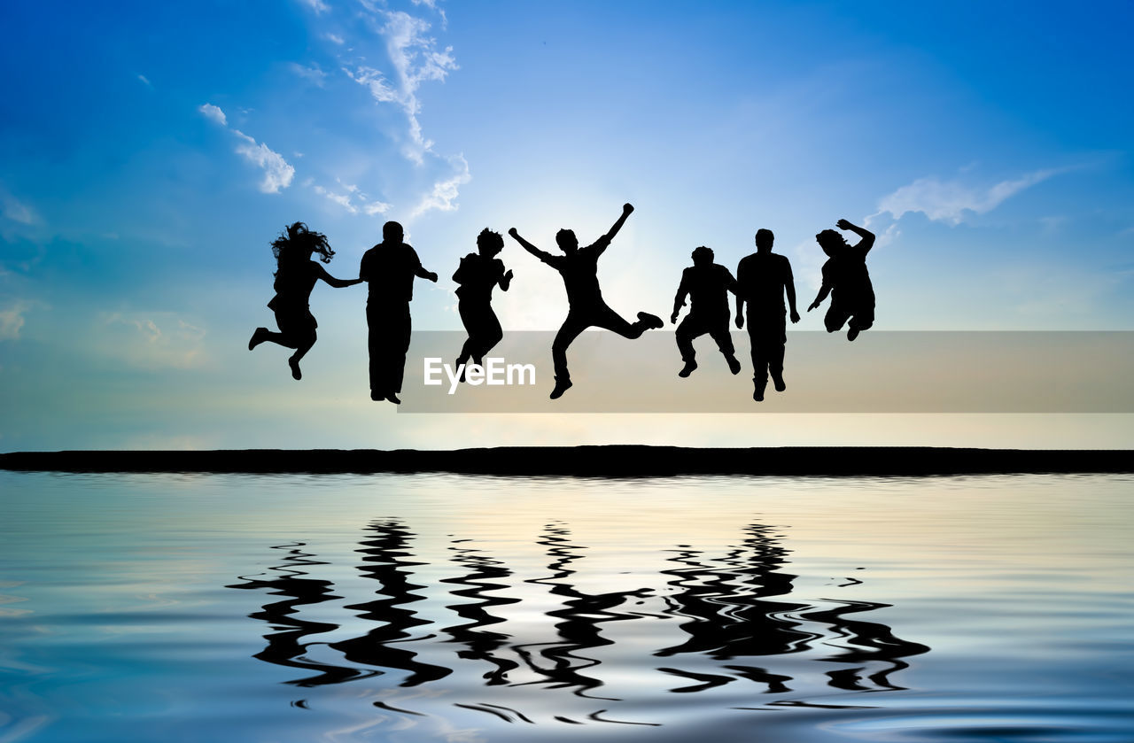 Silhouette people jumping over lake against sky during sunset