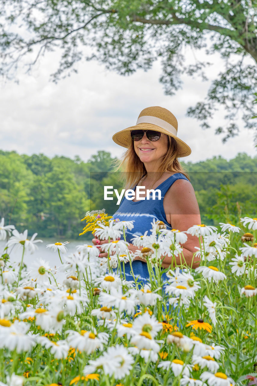 Smiling woman in hat standing by flowers