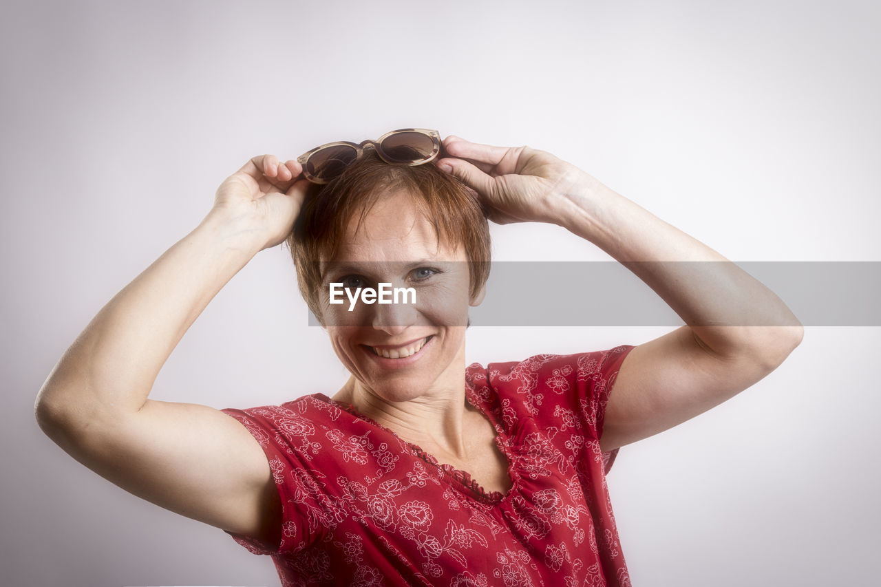 Portrait of happy mature woman wearing sunglasses against white background