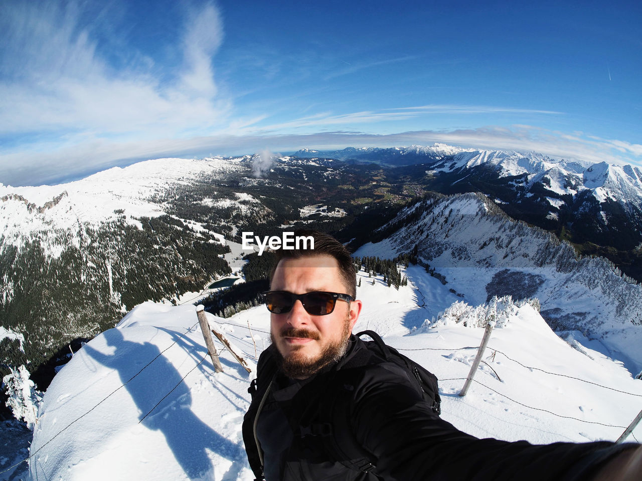 High angle portrait of man wearing sunglasses standing on snowcapped mountain