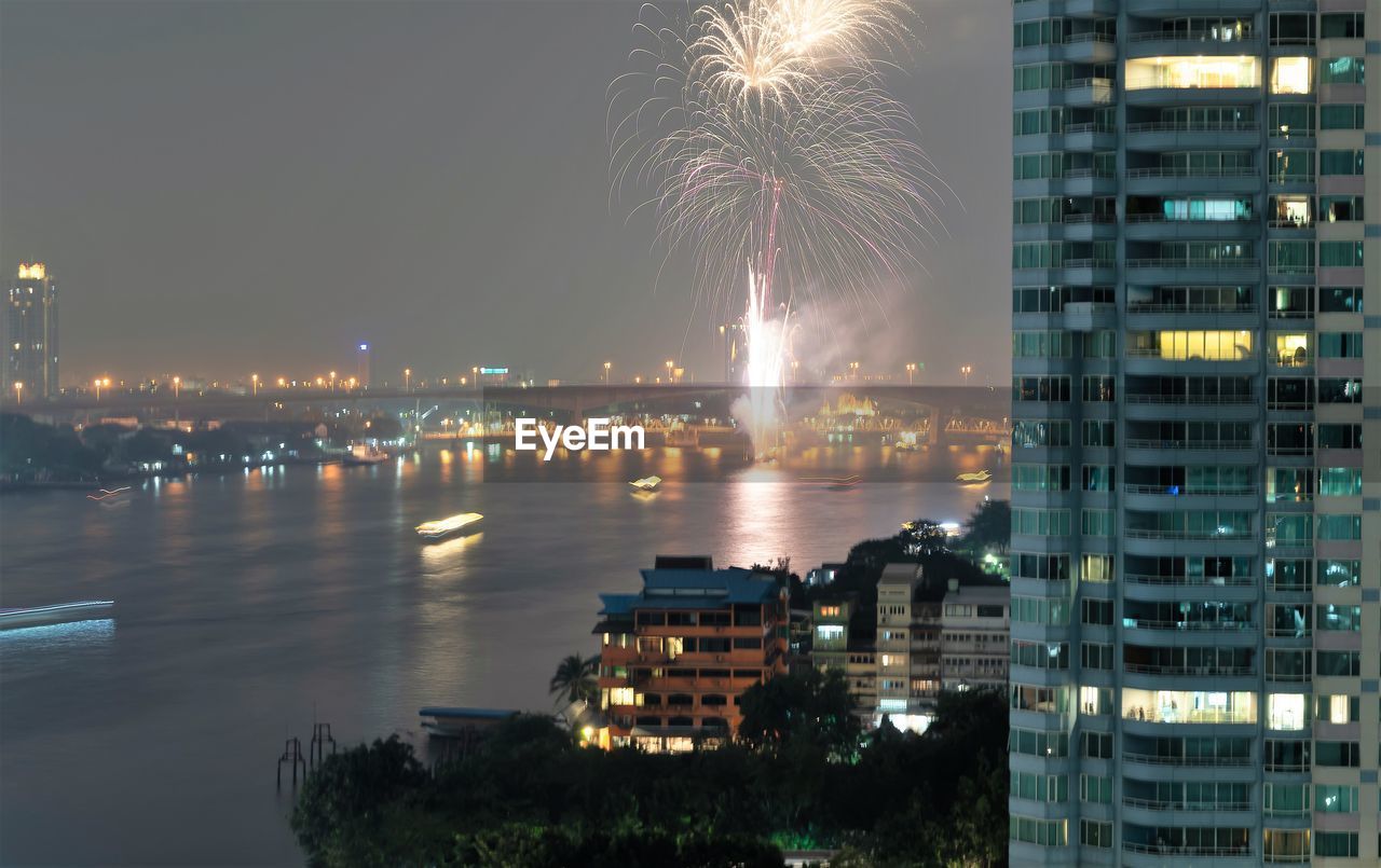 FIREWORK DISPLAY OVER RIVER AND BUILDINGS IN CITY