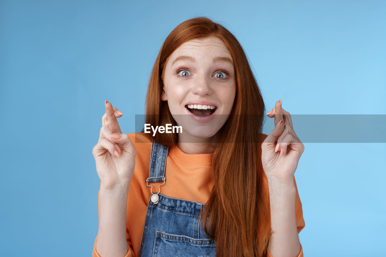 Happy woman with fingers crossed against blue background