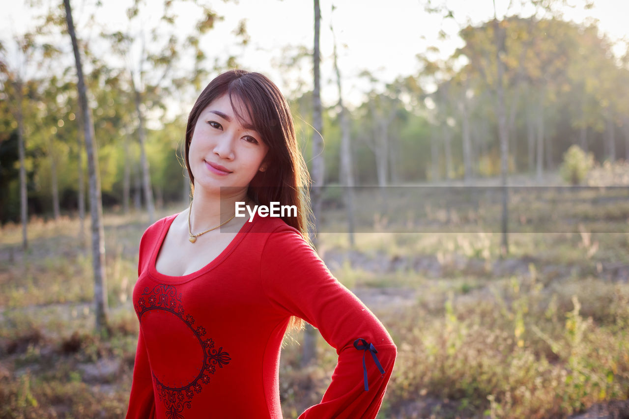 PORTRAIT OF BEAUTIFUL WOMAN STANDING AGAINST RED TREES