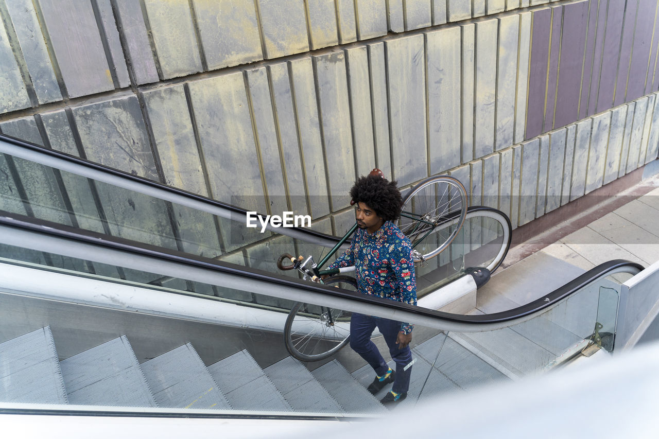 Stylish man carrying bicycle on escalator