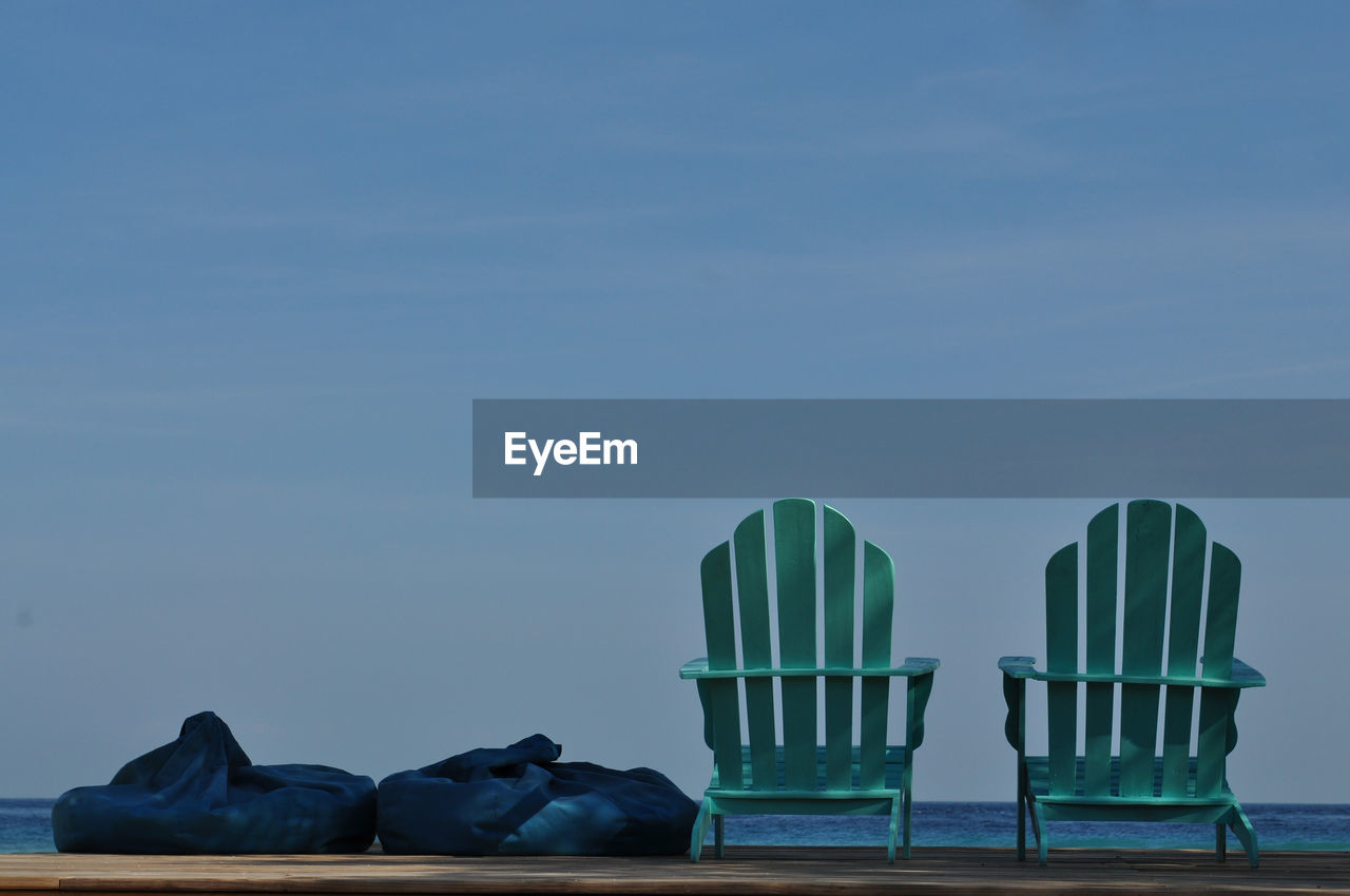 Adirondack chairs with bean bags on pier against sky