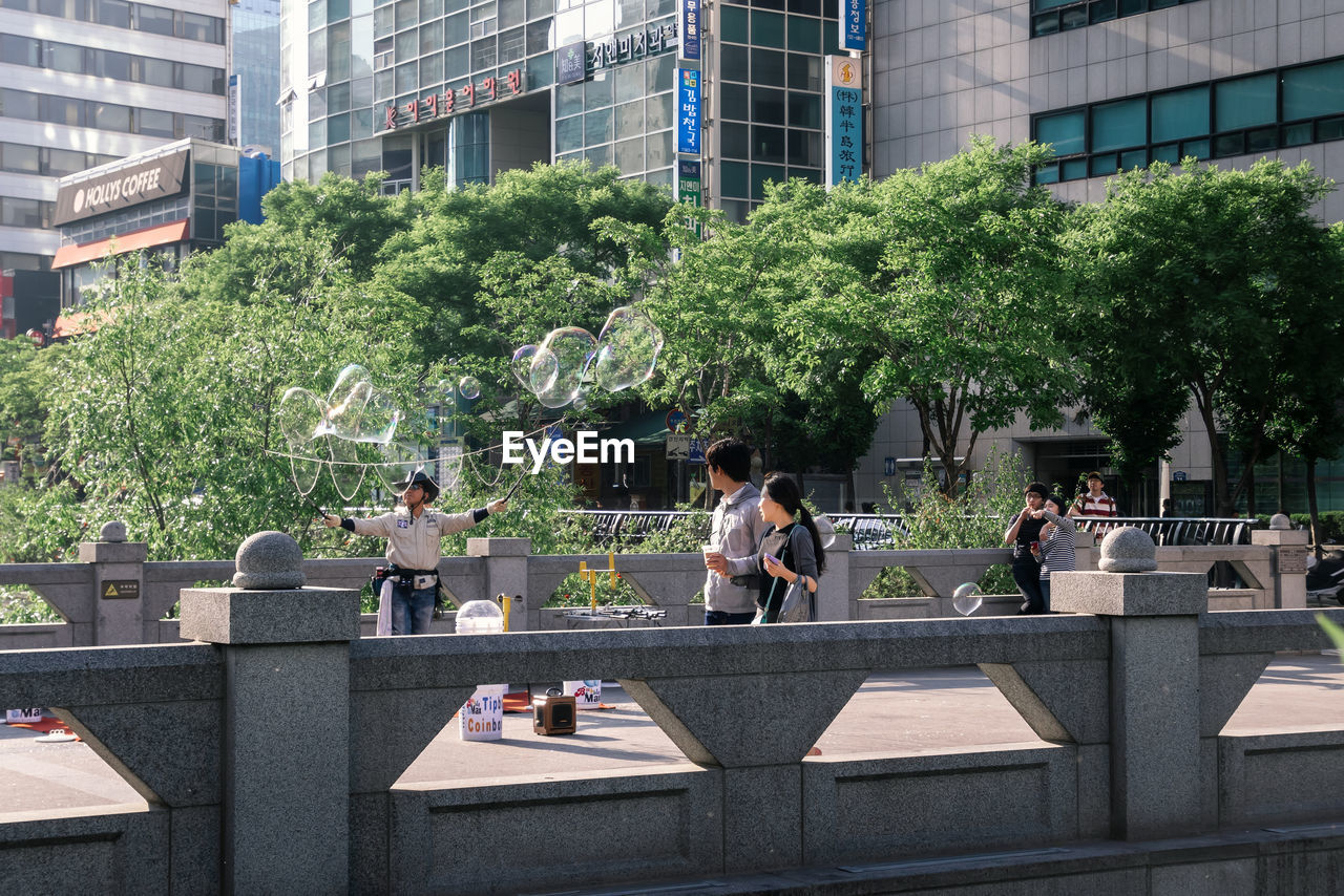 PEOPLE SITTING BY BUILDINGS IN CITY