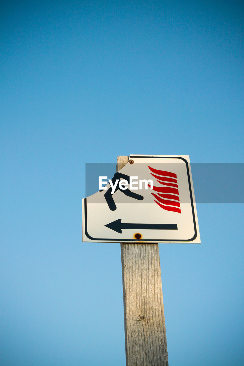 Low angle view of road sign against clear blue sky