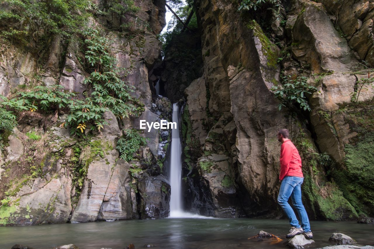 Man standing by waterfall in forest