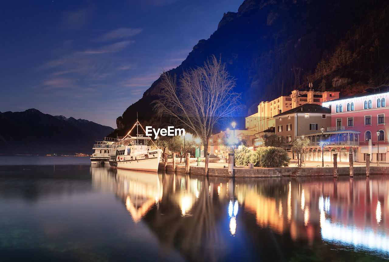 Illuminated buildings by lake against sky at night