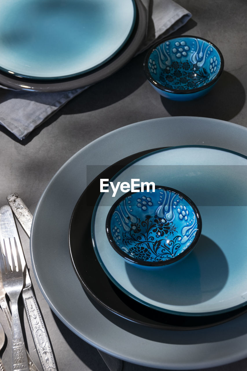 Tableware, different plates in grey blue colors on dark table with geometrical shapes shadows