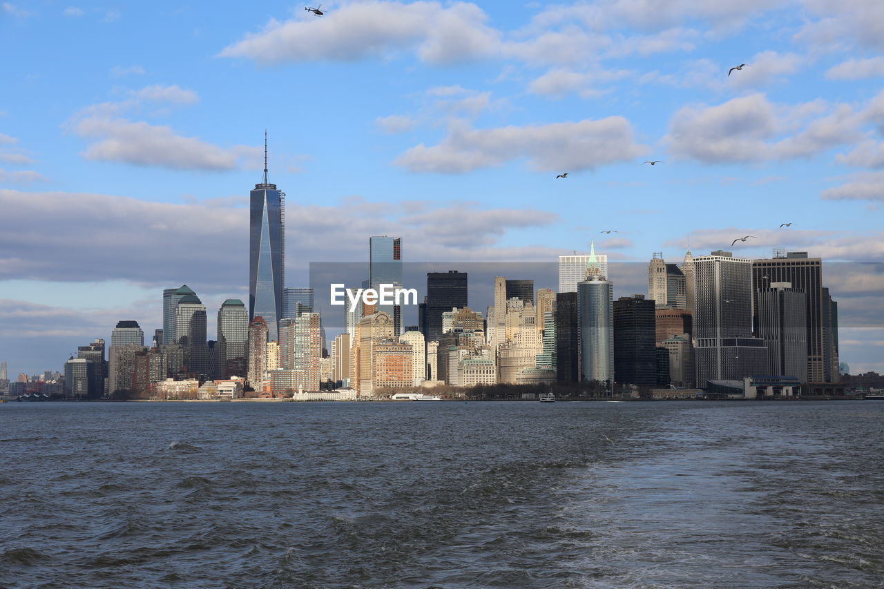 Sea by modern buildings against sky in city