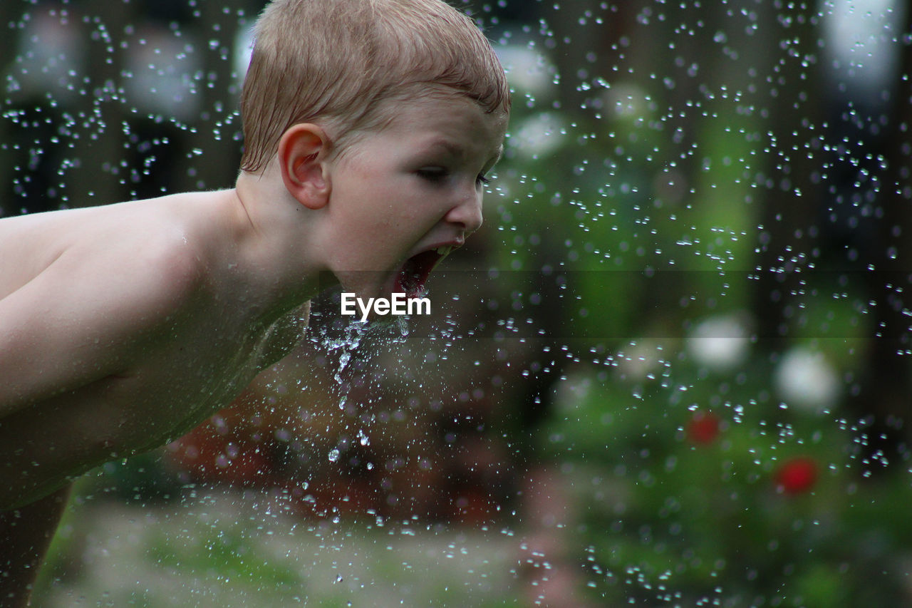 Close-up of shirtless boy playing with water in yard