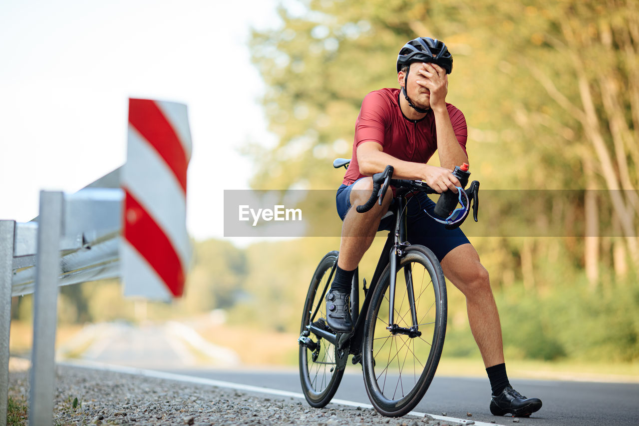 Professional cyclist in helmet feeling strong exhaustion after long morning ride on paved road. 