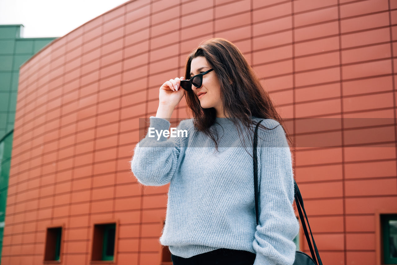 YOUNG WOMAN USING SMART PHONE AGAINST BRICK WALL