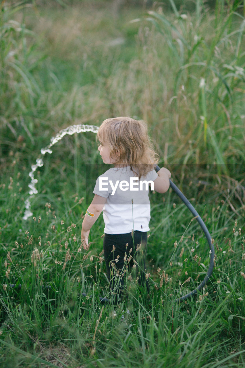grass, childhood, child, plant, one person, nature, green, meadow, blond hair, casual clothing, lawn, leisure activity, full length, day, land, flower, outdoors, field, standing, men, innocence, holding, rear view, women, lifestyles, motion, growth, female, emotion, water, toddler, fun, summer, hairstyle, three quarter length