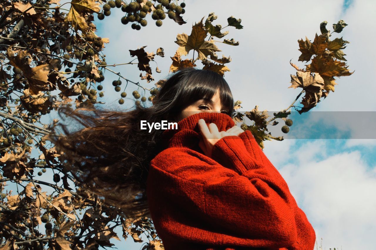 Low angle portrait of woman wearing warm clothing while standing against branches