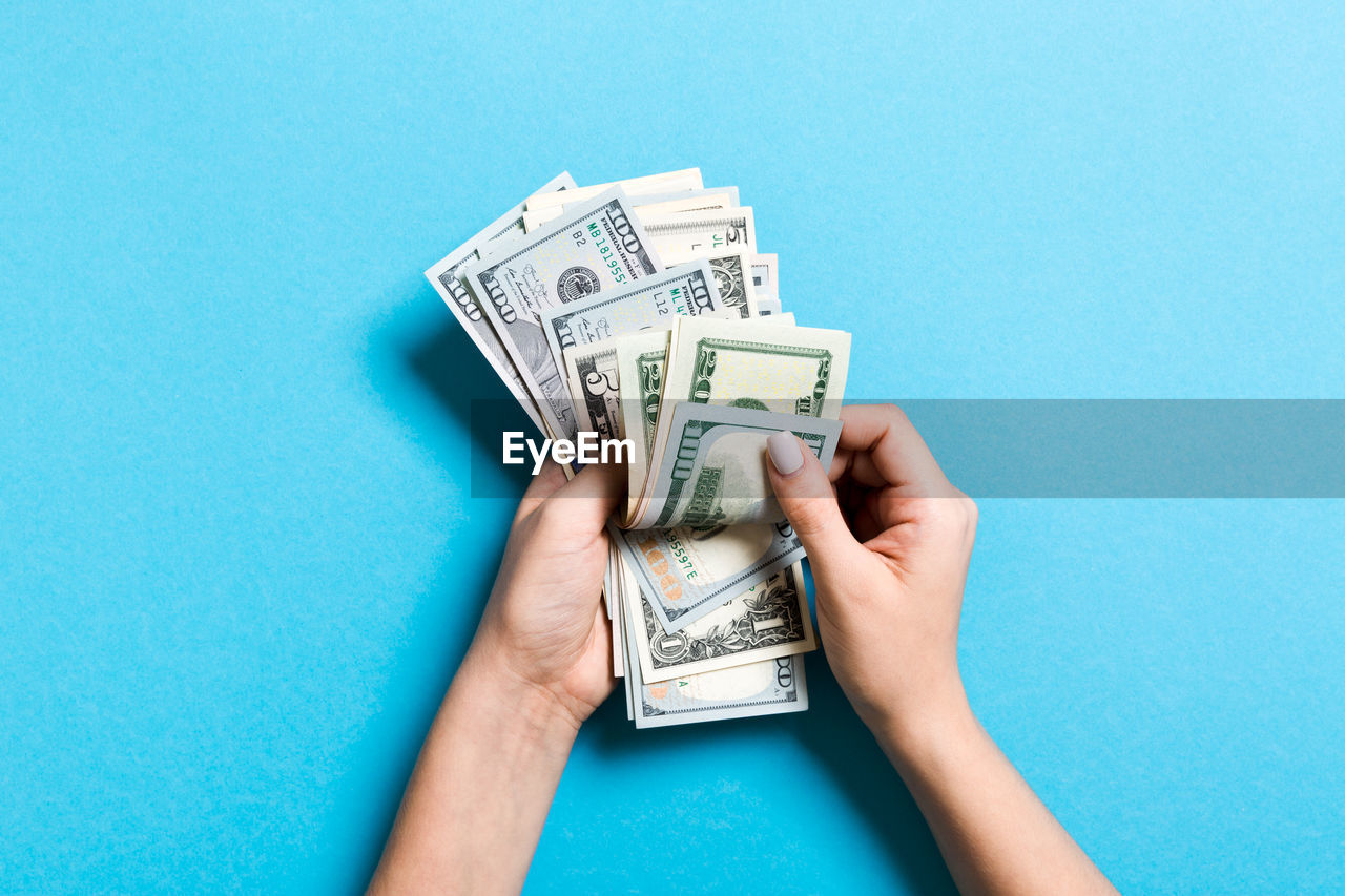 Close-up of hands holding paper currency against blue background